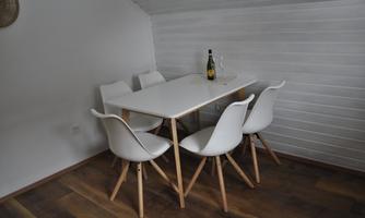 A modern dining area with a white table and four chairs. There is a bottle of sparkling wine on the table.
