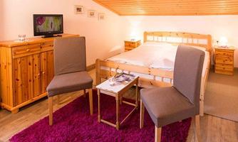 A cozy bedroom with a double bed, two chairs, and a small table. The room has a warm atmosphere with wooden furniture and a carpet.