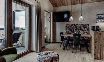 A modern living environment with wooden ceilings and elegant furnishings. The space features a dining table, chairs, and large windows with access to the balcony.