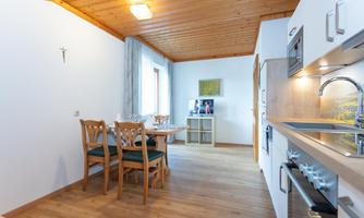 A bright, inviting kitchen with a dining area. The wooden floor and wooden ceiling create a cozy atmosphere.
