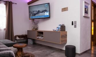 A modern living room with a flat-screen TV on the wall. The decor is simple and cozy, featuring a sofa and a small table.