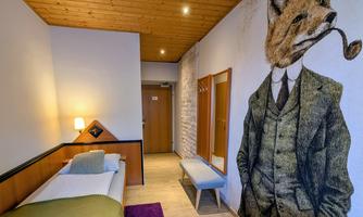 A stylish room with a wooden ceiling and a remarkable wall painting of a fox in a suit. There is a single bed, a table, and a carpet on the floor.