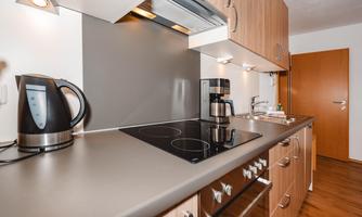 A modern kitchen with wooden cabinets and metal appliances. It is well-equipped with a stove, a kettle, and a coffee machine.
