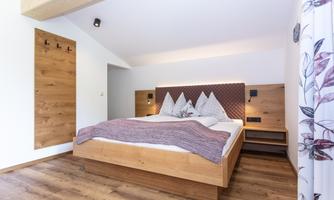 A modern bedroom with a wooden frame bed and cozy bedding. The walls are light and the decor is minimalist.