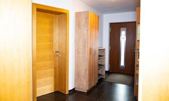 A bright hallway with wooden details and a modern wardrobe. The entrance door has a large window and the floor is dark tiles.