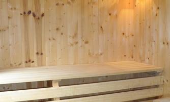 A wood sauna with benches and a small bucket. The light creates a relaxing atmosphere.