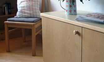 A cozy room with a wooden cabinet and a chair. On the table, there is a vase with red flowers.