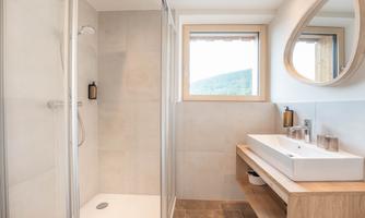 A modern bathroom with a shower and a large sink. The large windows provide plenty of daylight and a pleasant atmosphere.