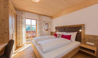 A cozy bedroom with a double bed and light wooden furniture. Generous windows allow for plenty of daylight and a view outside.
