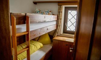 A cozy room with a wooden bunk bed. There is a window with a view outside and some pillows on the bed.