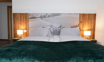 A cozy bedroom with a large double bed and a wooden screen. The nightstands are equipped with lamps and the comforter is in a soft green tone.