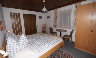 A cozy bedroom with two beds and checkered pillows. There is a small table, chairs, and a wardrobe.