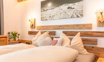 A cozy bedroom with two beds and wooden decor. A picture of snow-covered mountains hangs on the wall.