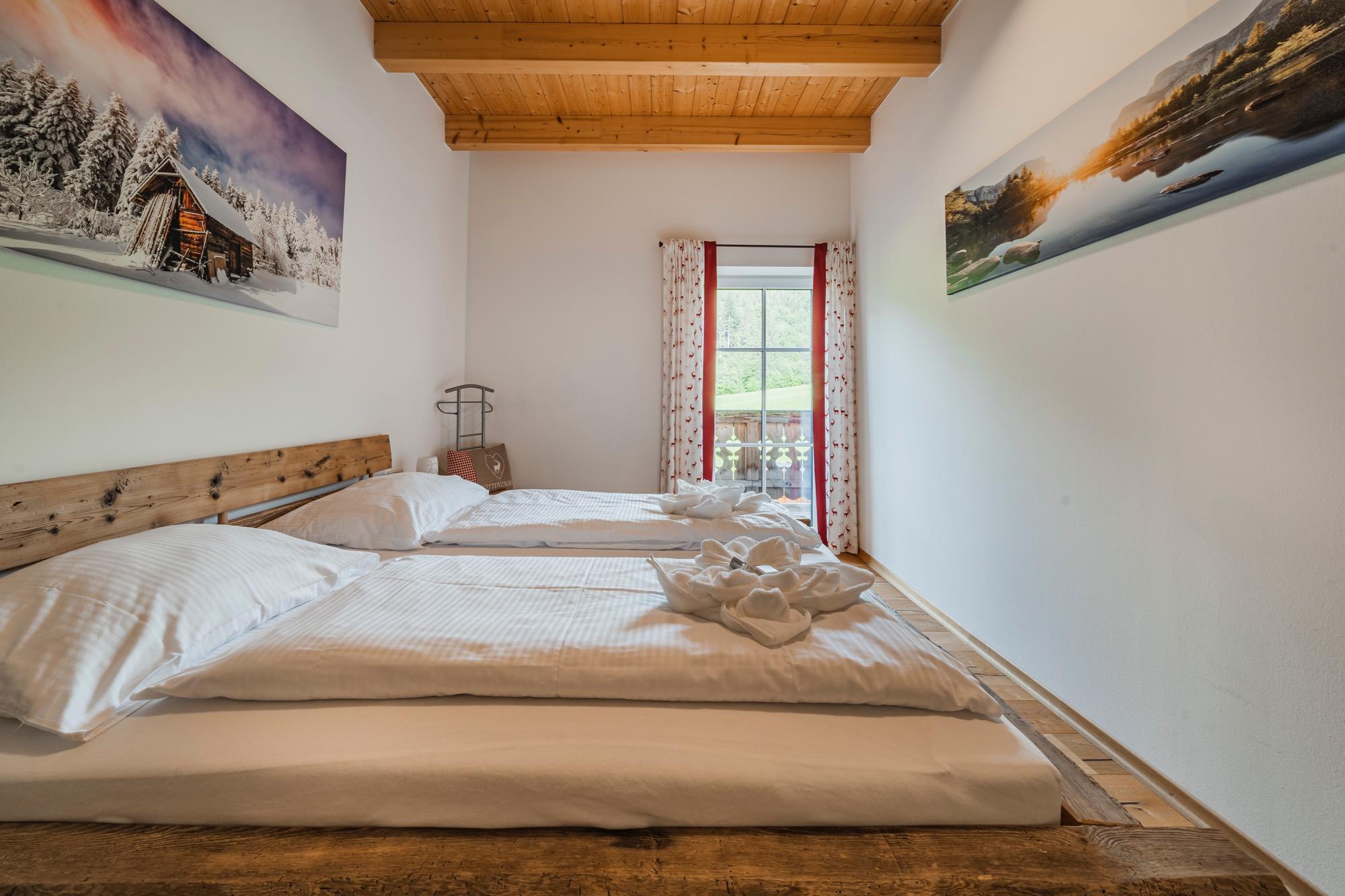 A cozy bedroom with two beds and natural wood. Large windows let in plenty of light and offer a view of the landscape.
