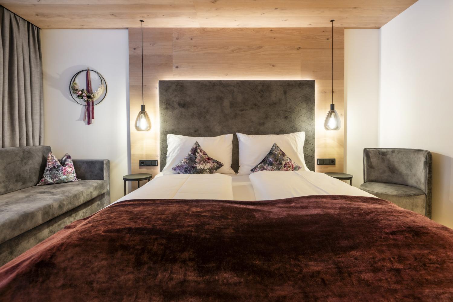 A modern bedroom with a large bed and cozy seating areas. The walls are light, and the wooden details create a warm atmosphere.