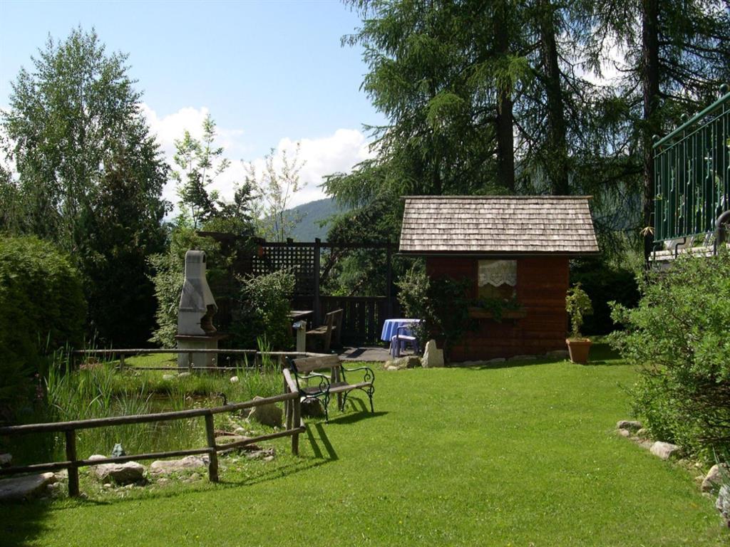 A beautiful garden with a small hut and green lawns. In the background, there are trees and a clear sky.