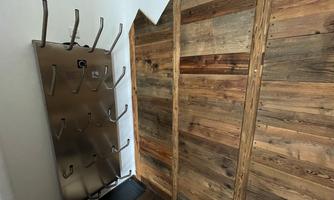 A simple entrance area with a wooden wall and a coat rack made of stainless steel. The floor is covered with a dark carpet.