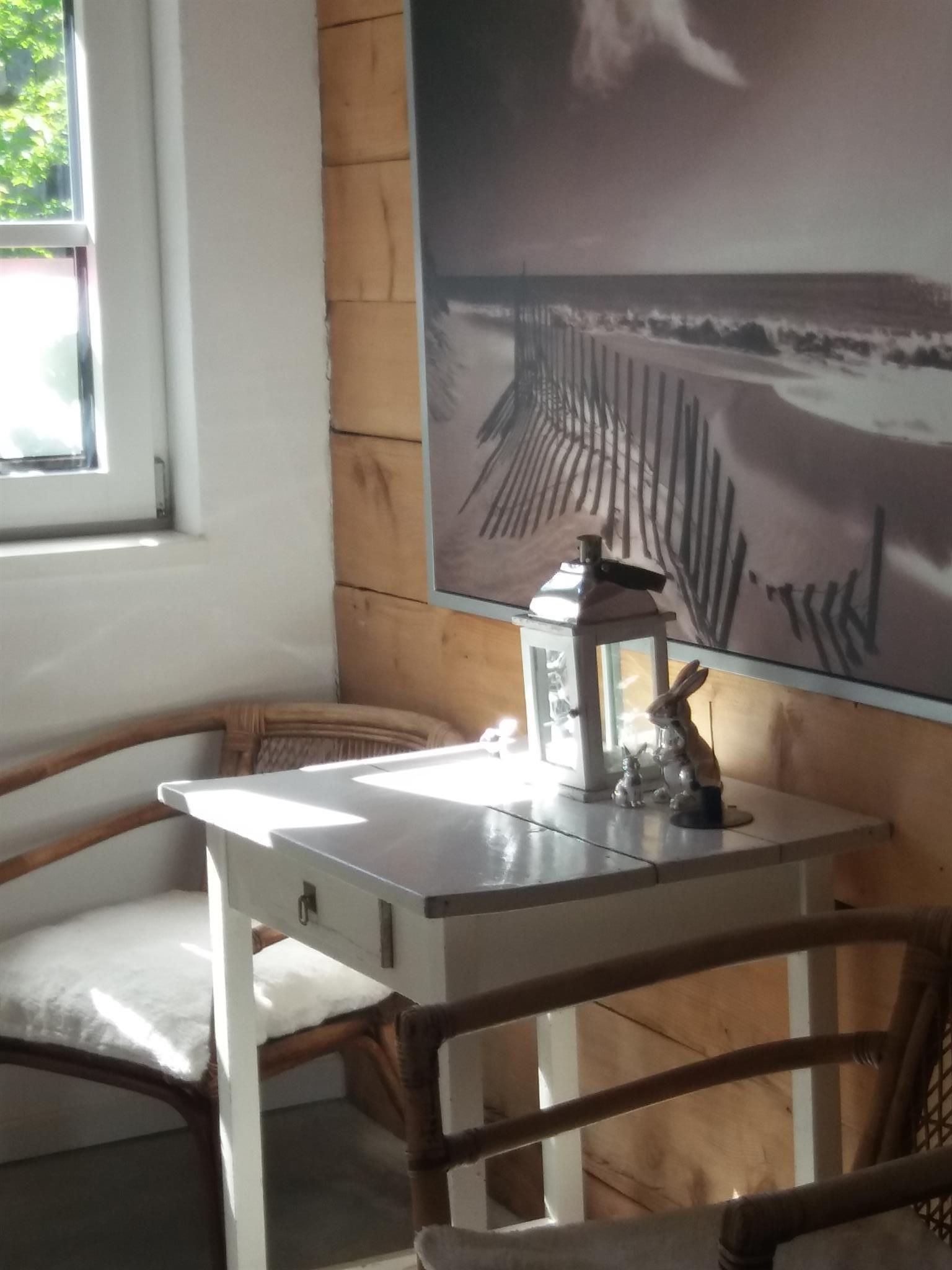 A cozy table with chairs in a bright room. A large picture of a beach with a fence in the sand hangs on the wall.