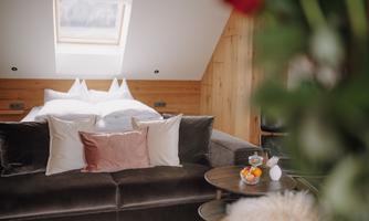 A cozy room with a large bed and a comfortable sofa. The room has a modern, warm style with wooden ceilings and natural elements.