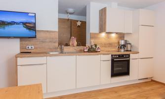 A modern kitchen with bright cabinets and wooden surfaces. A television is mounted on the wall, and the countertop is well decorated.