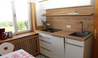 A modern kitchen with wooden shelves and an elegant sink. Windows provide a beautiful view of the outside.