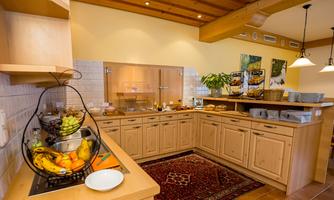 A bright kitchen with wooden cabinets and a fruit bowl. Various groceries and dishes are visible on the countertop.