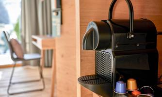 A black coffee machine is on a wooden table. Next to it, some coffee capsules in different colors are visible.