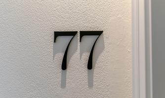 A wall with the number 77 in black writing. The digits are designed in a modern and clear style.