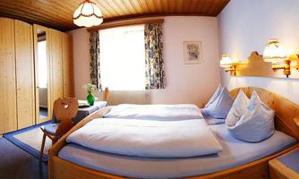 A cozy bedroom with a large double bed and blue pillows. The warm wooden furniture and soft lighting create an inviting atmosphere.