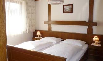 A cozy bedroom with a double bed and bright pillows. Small nightstands with lamps and a window that lets in daylight.