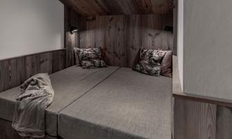 A cozy bedroom with two beds and wood paneling. Decorative cushions and a blanket give the room a warm atmosphere.