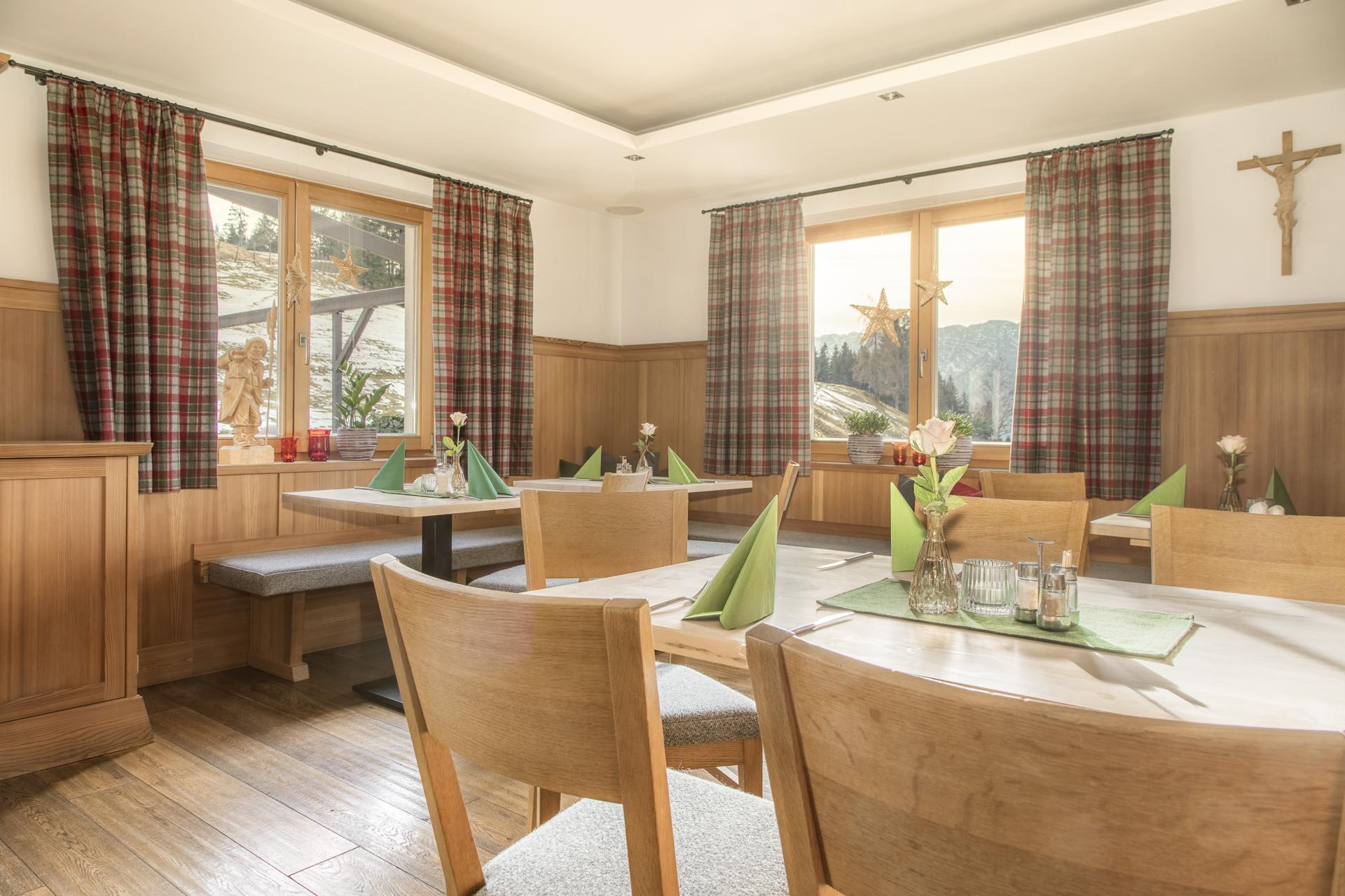 A cozy dining room with wooden furniture and large windows. The tables are adorned with green napkins and decorative flowers.