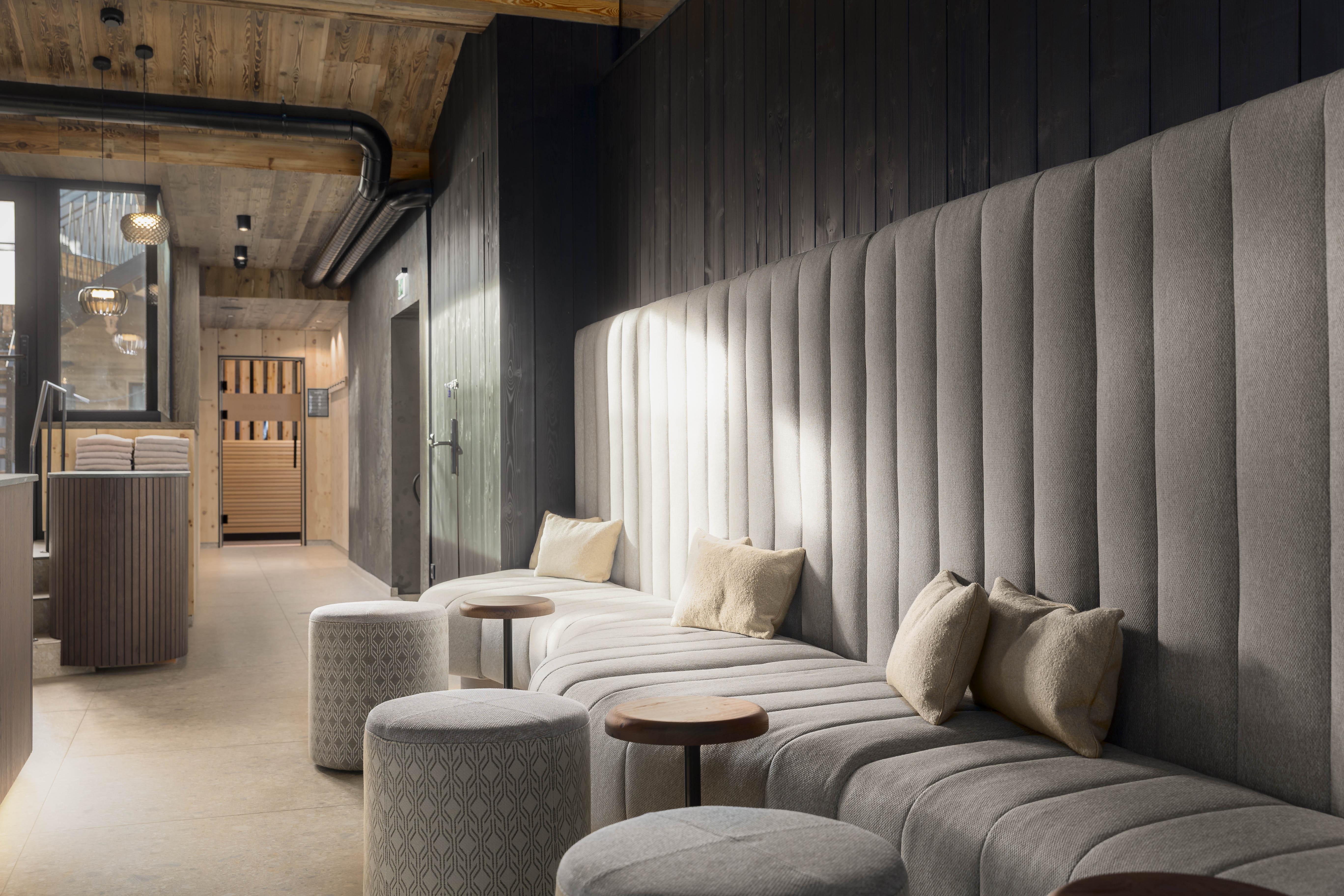 An elegant lounge area with upholstered benches and stylish stools. The ambiance is modern and inviting, featuring wooden details and soft lighting.