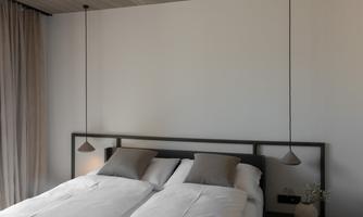 A modern bedroom with a double bed and minimalist decor. Soft light sources and bright colors create a relaxed atmosphere.