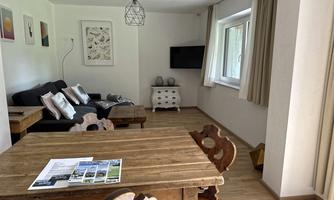 A bright living room with a cozy sofa and a wooden table. There is a television and large windows that provide plenty of daylight.
