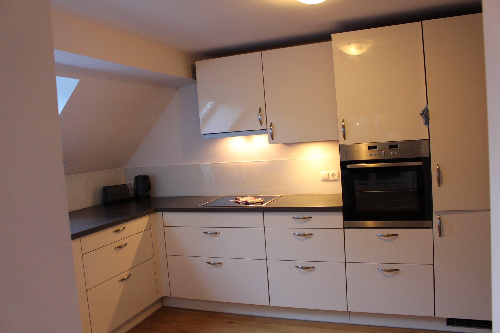 A modern kitchen with white furniture and a stove. There is an oven and plenty of storage space under the countertop.
