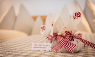 A decorative gift on a bed with a note that says "especially for you, sleep well." The gift consists of a white cloth with red embellishments and a checked ribbon.
