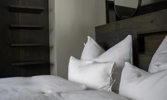 A modern bedroom with white pillows and a minimalist wooden structure. The simple decor exudes tranquility and coziness.