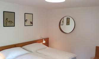 A cozy bedroom with a double bed and two nightstands. Pictures of birds are hanging on the wall, as well as a round mirror.