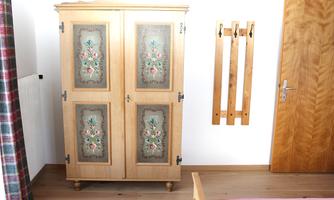 A beautiful, vintage wardrobe with colorful embellishments stands in a bright room. Wooden coat hooks hang on the wall next to a door.