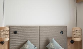A modern bedroom with a large bed, cozy pillows, and wooden accents. The lighting is soft and creates a relaxed atmosphere.