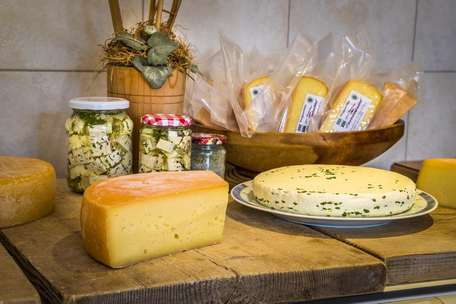 A tray with various types of cheese and pickled cheese in jars. The cheeses are arranged on wooden surfaces.