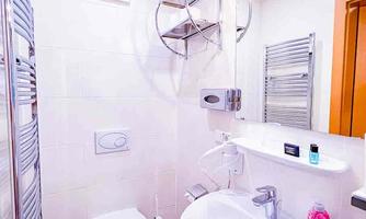 A modern bathroom with a sink, toilet, and towel radiator. The walls are bright, and the furnishings are simple and functional.
