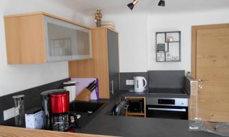 A modern kitchen with wood and gray elements. It is equipped with a refrigerator, a kettle, and an oven.