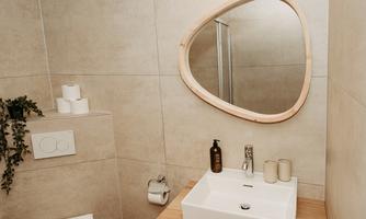 A modern bathroom with simple grey walls and wooden details. The sink area is neatly arranged with a stylish round mirror surface and decorative items.