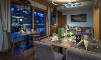 A cozy restaurant with modern wooden tables and elegant decoration. Large windows offer a view outside, while gentle light installations create an inviting atmosphere.
