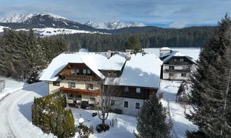 A picturesque winter village with snow-covered houses. In the background, majestic mountains and a clear sky can be seen.