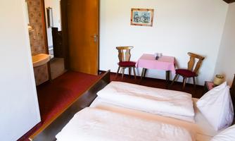A simple room with two beds, a table, and chairs. In the background, a bathroom is visible.