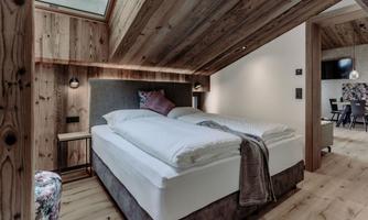 A cozy bedroom with wooden paneling and a large double bed. The room has large windows that provide plenty of daylight.