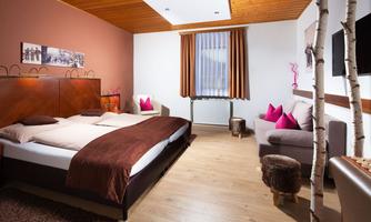 A modern hotel room with a double bed and a cozy sofa. The walls are painted in warm colors and there are some decorative pillows.